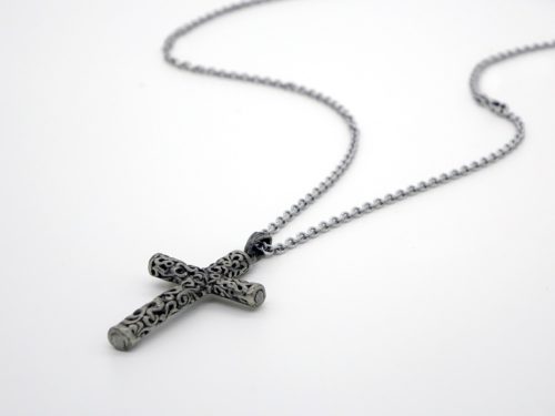 An ornate silver cross pendant with intricate detailing, symbolizing faith, hangs from a silver chain. The necklace is laid out on a white background, highlighting the exquisite design of the religious emblem.