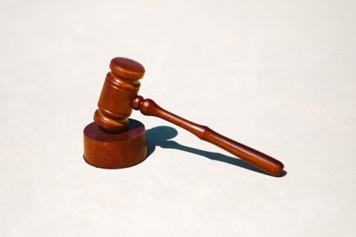 A wooden gavel and sound block rest on a light surface, a shadow cast to the right. The gavel lies with its handle on the right, embodying justice akin to the discipline and order found in military service.